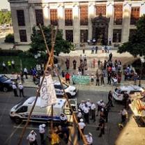 Crowd of protestors outside a big government building with a tripod looking wooden structure in the street