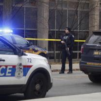 Police car and officer with gun outside building with crime tape around it