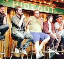 Different sizes and types of white guys sitting on stools on a stage, a couple talking into mics