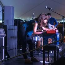 Dark haired woman leaning over a keyboard with a band on a stage