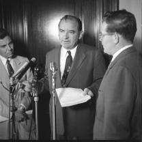 McCarthy talking at a microphone 