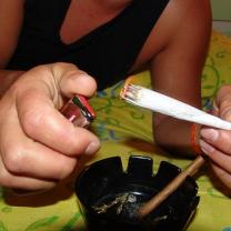 Person's hands lighting a huge joint over an ashtray